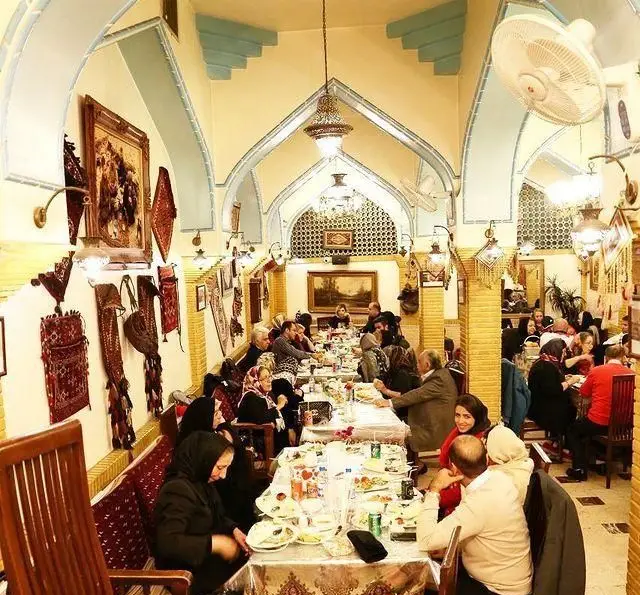 فضای دلنشین سفره خانه سنتی باغ فردوس با مشتریان در حال صرف غذا، دکوراسیون سنتی ایرانی و معماری زیبای طاق‌ها و روشنایی.
