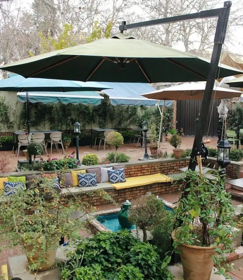 فضای دلنشین کافه تی آرت با حیاطی سرسبز، میز و صندلی‌های شیک زیر چترهای بزرگ، و حوضچه ای زیبا برای آرامش مهمانان.