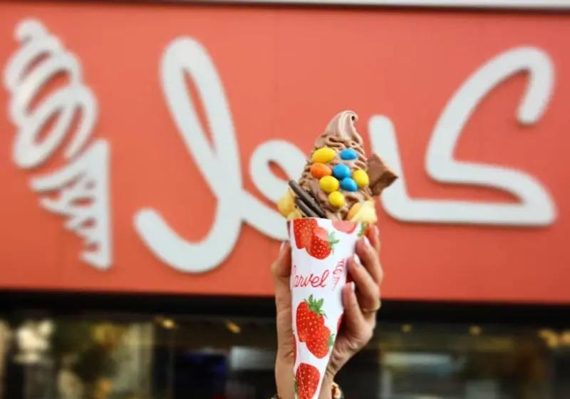 بستنی وافل حبابی شکلاتی خوشمزه کارول با ام اند امز رنگی و تزیینات، در دست مشتری مقابل لوگوی جذاب کارول.