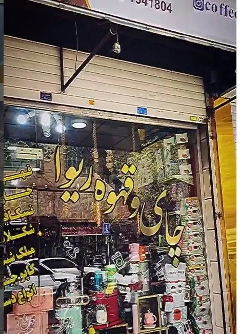 نمای بیرونی کافه ریوا با ویترین پر از انواع چای، قهوه، نسکافه، شکلات، میلکشیک و دسر، آماده پذیرایی از مشتریان است.