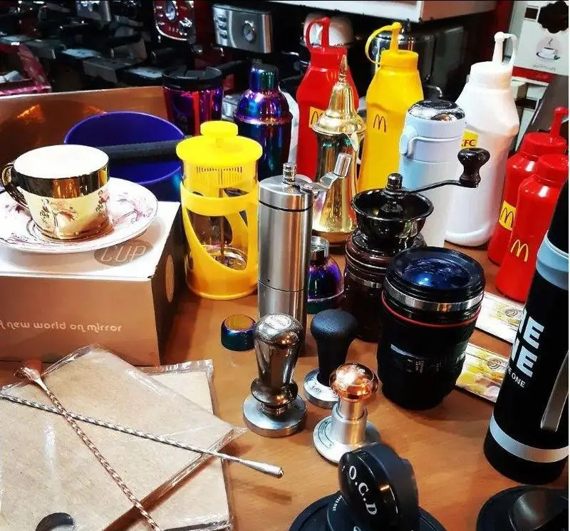 تصویری از تنوع بالای ابزارهای حرفه‌ای کافه ریوا: از آسیاب‌های قهوه و فرنچ پرس تا تمپر و فنجان‌های شیک برای باریستا.