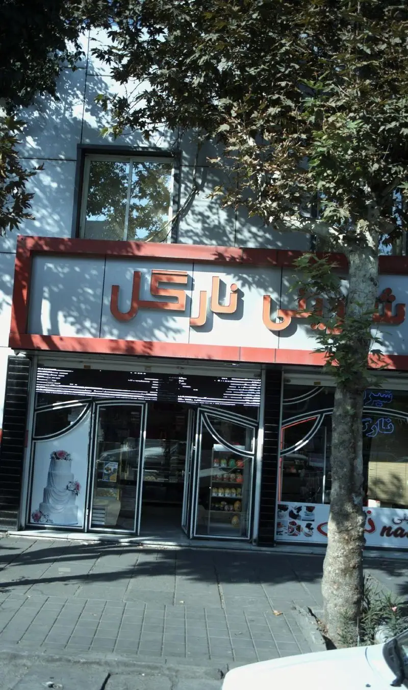 نمای بیرونی شیرینی نارگل، یک قنادی با تابلو نارنجی و درب‌های شیشه‌ای که کیک عروسی و دسرها را به نمایش می‌گذارد.