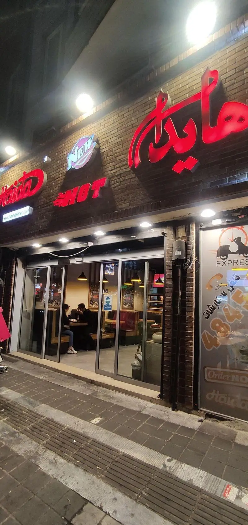 ساندویچ هایدا در شب، نمای بیرونی شعبه با تابلوهای نئونی درخشان "هایدا" و "New HOT". شامل خدمات اکسپرس و سفارش آنلاین.