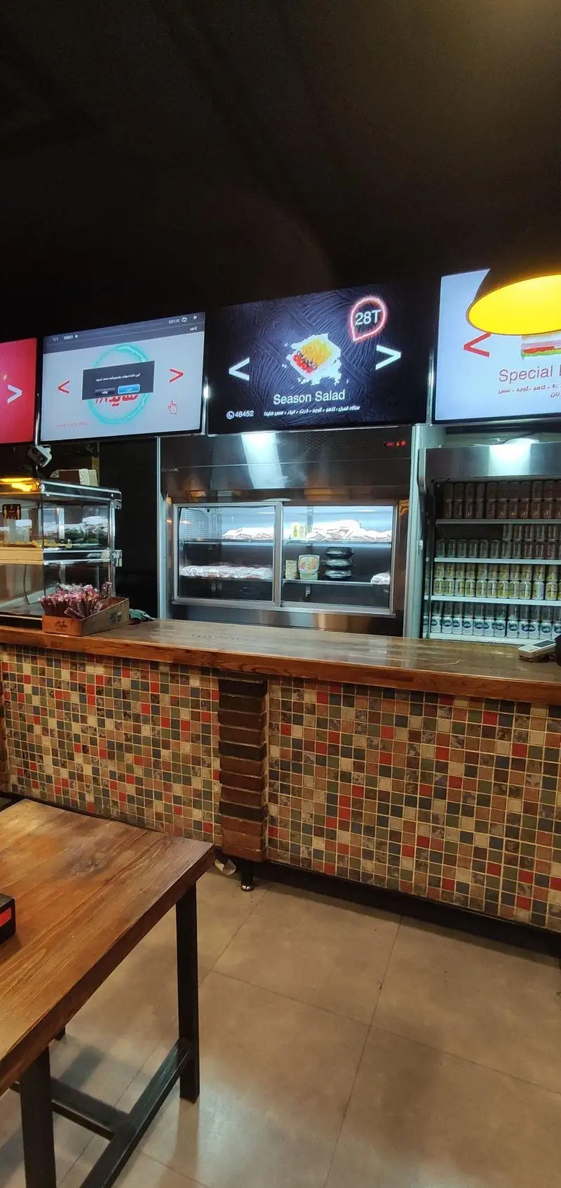 فضای داخلی ساندویچ هایدا با پیشخوان مدرن کاشی‌کاری شده، نمایشگرهای منوی دیجیتال شامل سالاد فصل و نوشیدنی‌های متنوع.