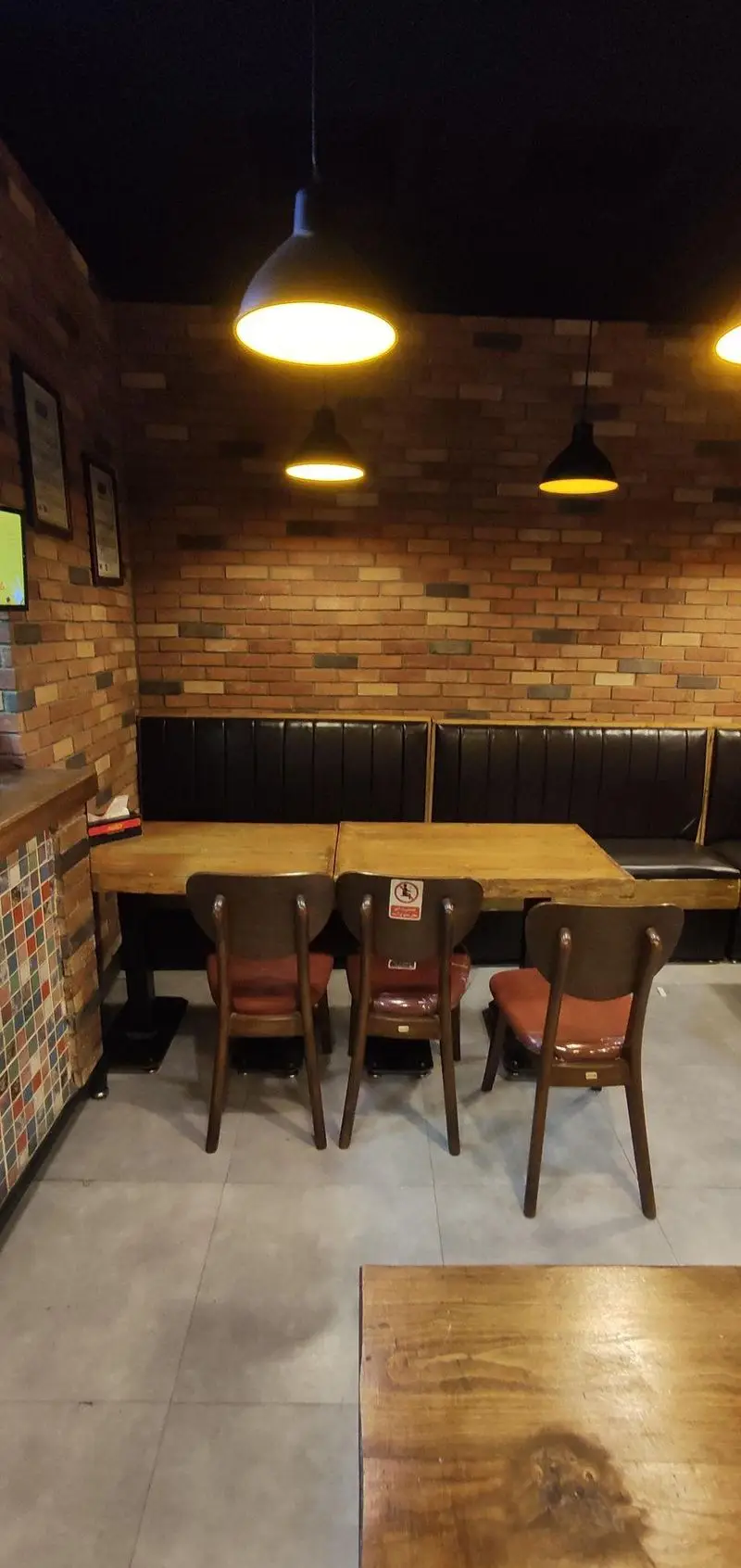 فضای داخلی ساندویچ هایدا: دیوارهای آجری، میز و صندلی چوبی قهوه‌ای با کوسن‌های قرمز، نیمکت‌های تیره، چراغ‌های آویز گرم. محیطی دنج برای مشتریان.