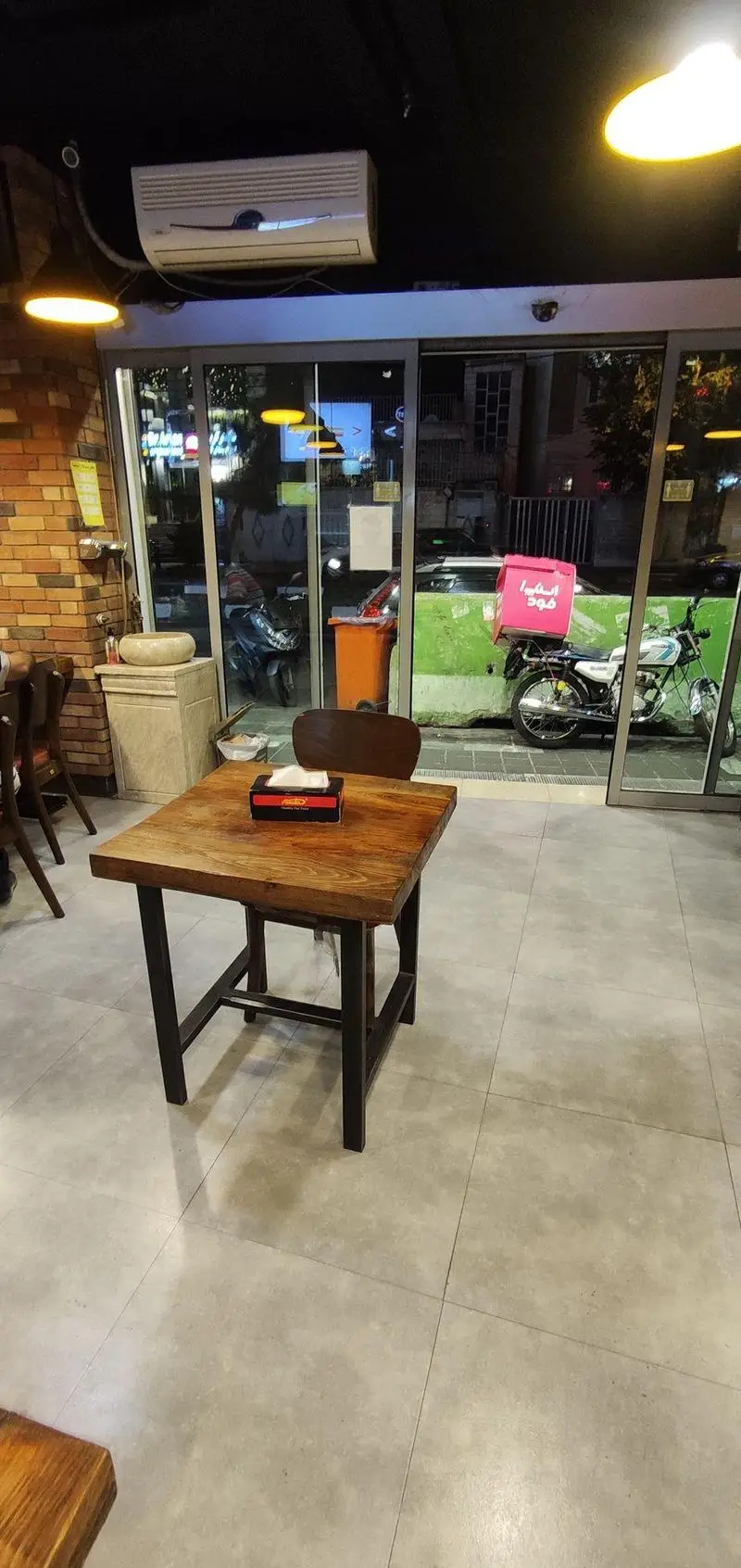 فضای داخلی مدرن و دلنشین ساندویچ هایدا، با میز چوبی، کفپوش روشن و دکوراسیون شیک. نمای خیابان با موتورسیکلت اسنپ فود، گویای خدمات سریع بیرون‌بر هایدا.