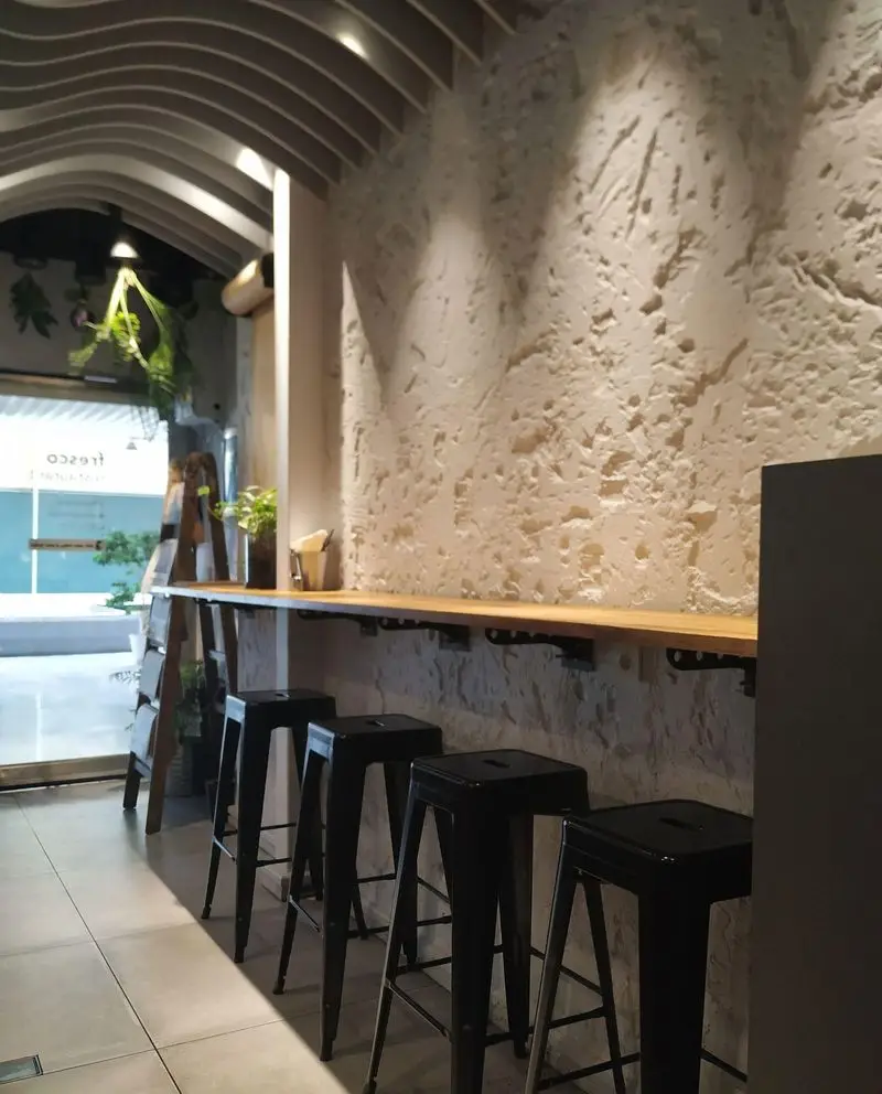 فضای دلنشین رستوران فرسکو با کانتر چوبی، صندلی‌های بار مشکی، دیوار بتنی طرح‌دار و سقف نوآورانه؛ محیطی ایده‌آل برای مشتریان.