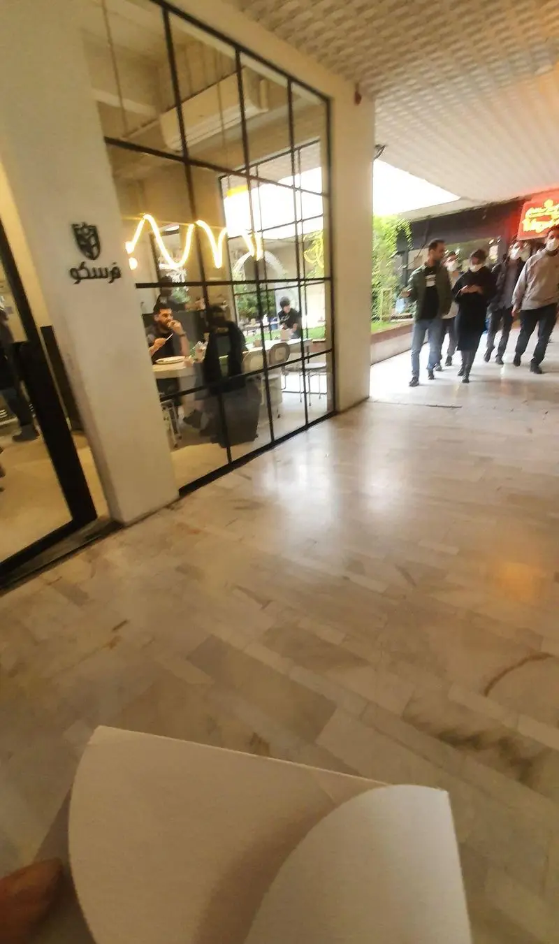 نمای ورودی رستوران فرسکو با پنجره‌های شیشه‌ای بزرگ، مشتریان در حال غذا خوردن داخل و افراد در حال تردد بیرون، محیطی دلنشین را نشان می‌دهد.