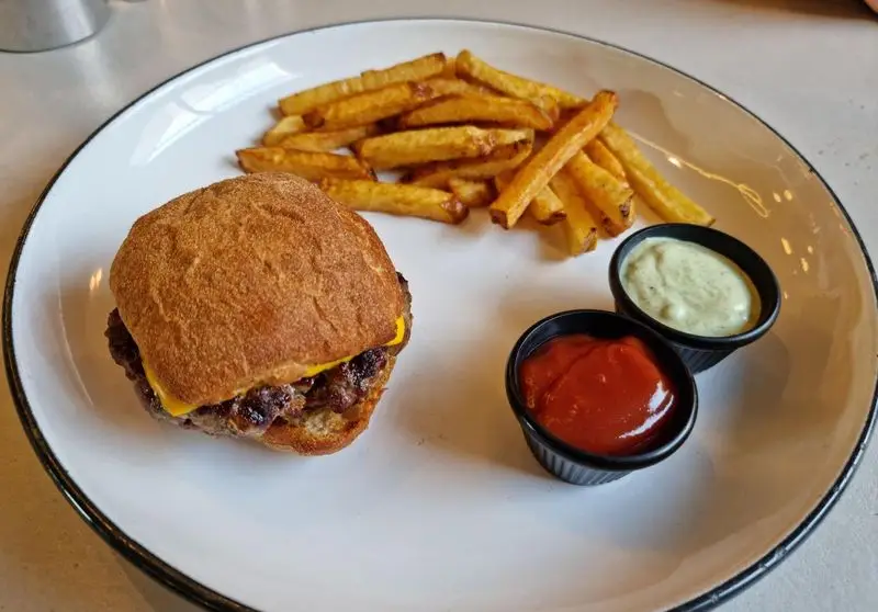 یک بشقاب غذای لذیذ فست فود از رستوران فرسکو: برگر کوچک آبدار با پنیر، سیب زمینی سرخ کرده ترد و طلایی، به همراه دو سس.