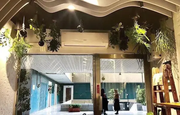 نمای داخلی و ورودی رستوران فرسکو با دکوراسیون مدرن، گیاهان آویزان، سقف موج دار و چشم انداز حیاط دلنشین