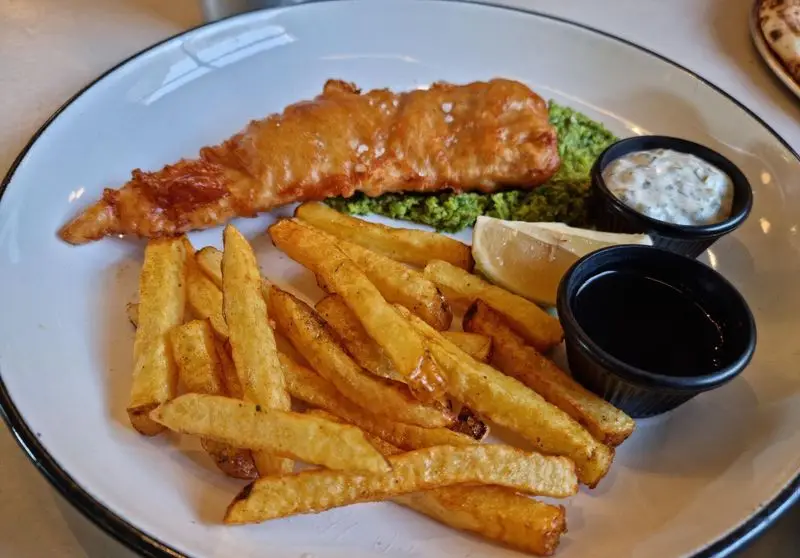 یک پرس فیش اند چیپس خوشمزه شامل ماهی ترد و طلایی، سیب زمینی سرخ کرده، نخود پوره، سس تارتار و لیمو در رستوران فرسکو.