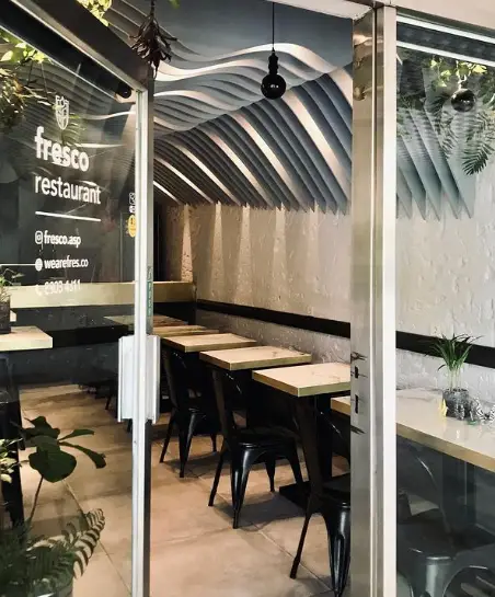 تصویری جذاب از ورودی و فضای داخلی رستوران فرسکو. سقف موج‌دار زیبا، میز و صندلی‌های شیک و دکوراسیون مدرن این رستوران.