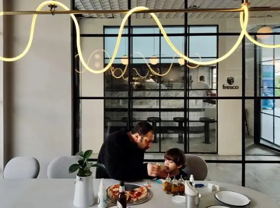 پدر و فرزندی در حال صرف پیتزا در رستوران فرسکو با طراحی داخلی مدرن و شیک. محیط خانوادگی برای لذت بردن از غذا.