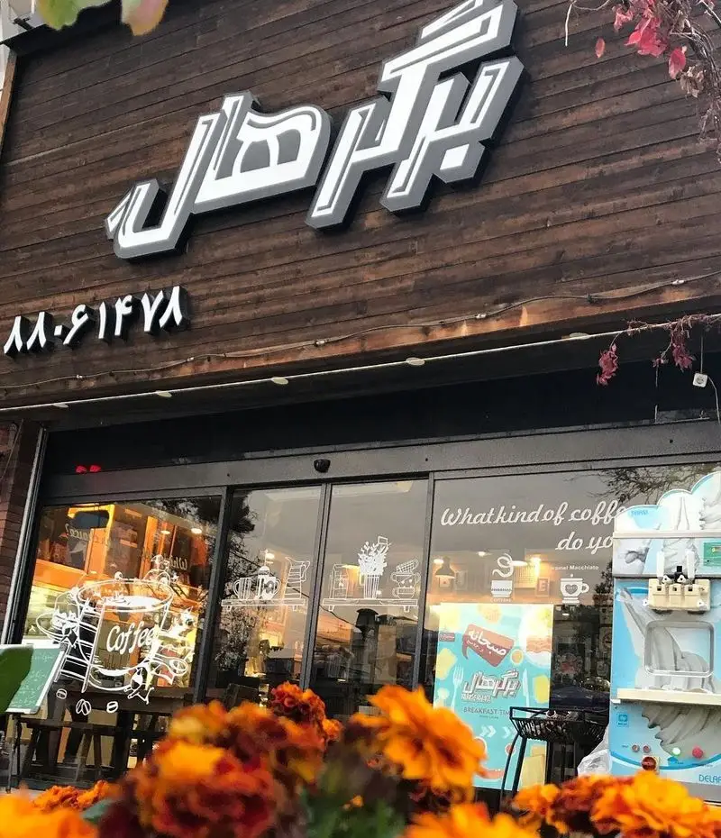 نمای بیرونی فست فود و کافه برگر هال با تابلوی روشن لوگو، نمای چوبی جذاب و ورودی شیشه‌ای که پیشنهاد صبحانه و قهوه را نشان می‌دهد.