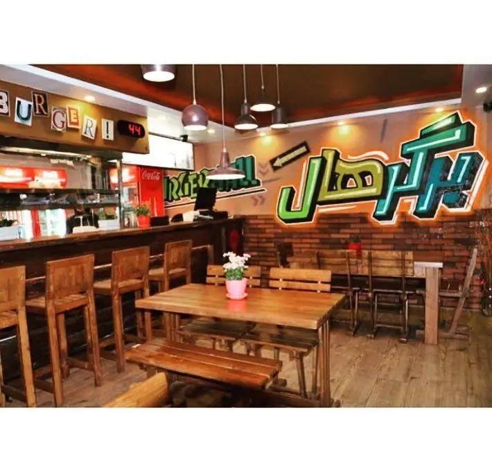 محیط داخلی فست فود برگر هال با طراحی مدرن و چوبی، کانتر و میز و صندلی‌های جذاب برای تجربه بهترین همبرگرها.