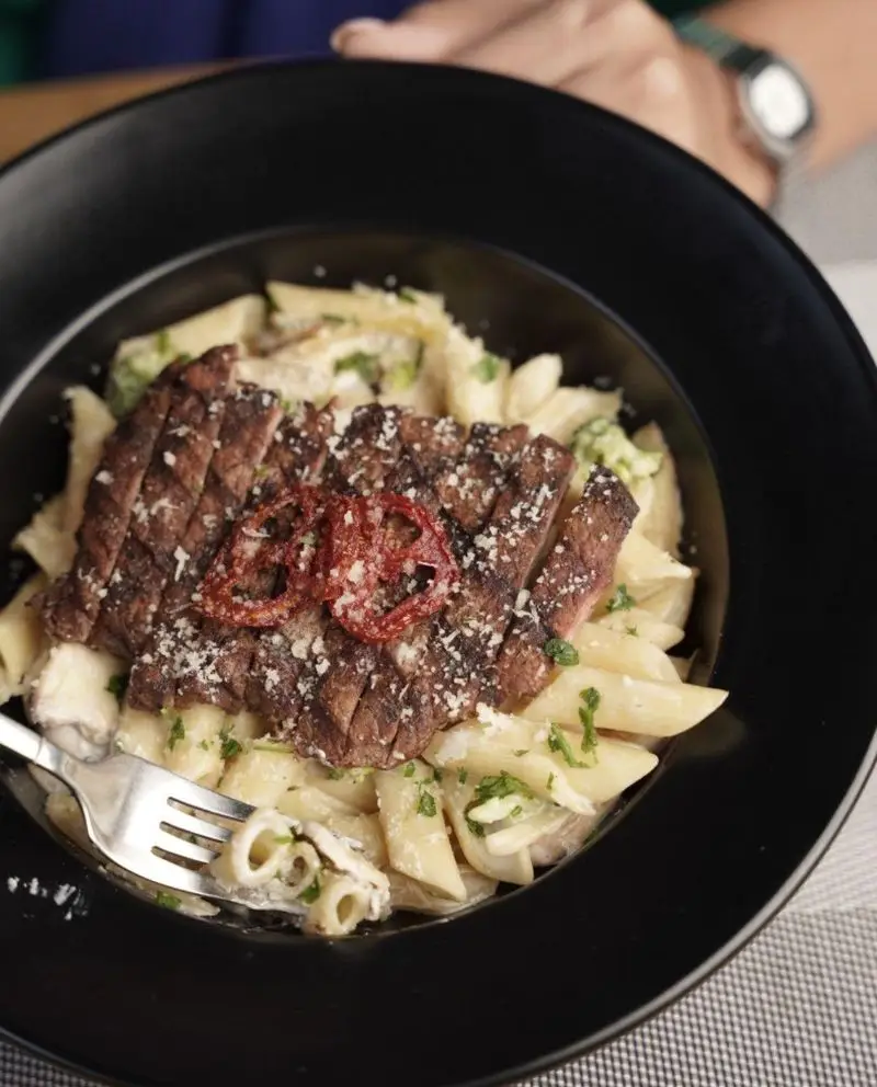 پاستا پنه با استیک گریل شده و سس خامه ای در ظرف مشکی، یک غذای خوشمزه و پرطرفدار از منوی فست فود د ل پ برای سرو در رستوران.