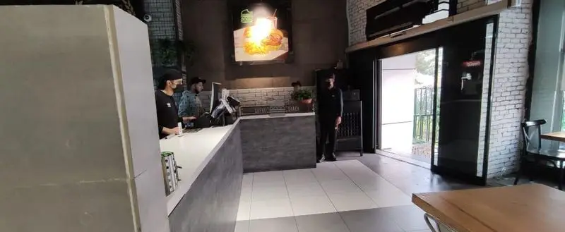 فضای داخلی مدرن و جذاب رستوران فست فود شیک شک، با کارکنان مشغول کار پشت پیشخوان، نمایشگر بزرگ منوی برگر و نوشیدنی.