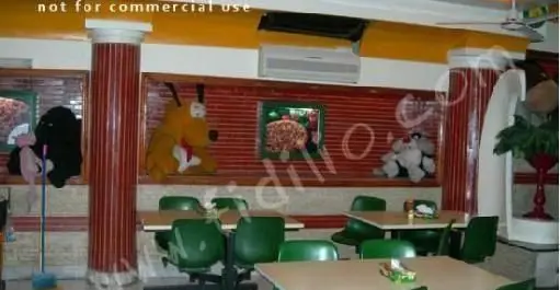 فضای دلنشین داخلی پیتزا مدبر با میز و صندلی‌های مدرن سبز، ستون‌های تزئینی و عروسک‌های بزرگ، مکانی ایده‌آل برای صرف پیتزا.