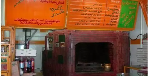 دکوراسیون داخلی پیتزا فروشی مدبر با تابلوهای منوی نارنجی رنگ به زبان فارسی و توضیحات اقلام غذایی نظیر پیتزا و ساندویچ، همراه با یک تنور سنتی آجری در مرکز.