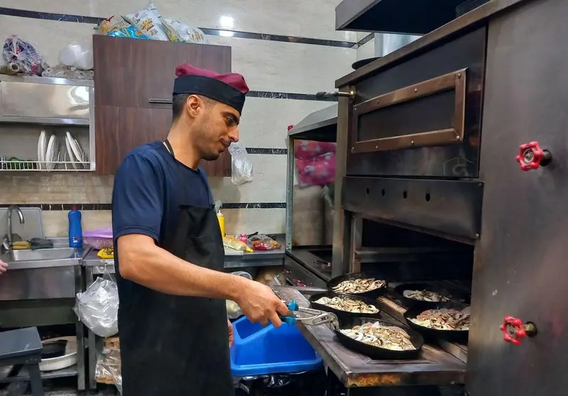 آشپز حرفه ای فستفود گل رز مشغول آماده سازی پیتزاهای قارچ در سینی های مخصوص، کنار فر بزرگ آشپزخانه. غذای با کیفیت.