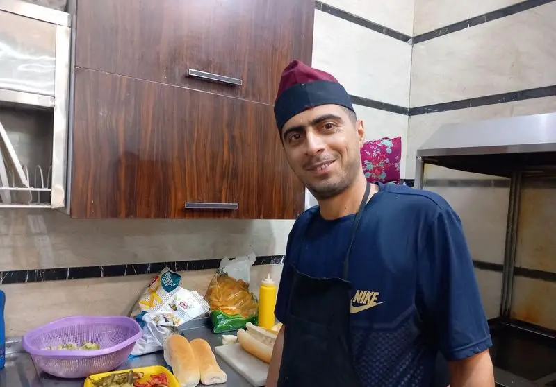 آشپز فستفود گل رز با لبخند در حال تهیه ساندویچ و غذا. مواد تازه و نان آماده برای مشتریان در آشپزخانه.