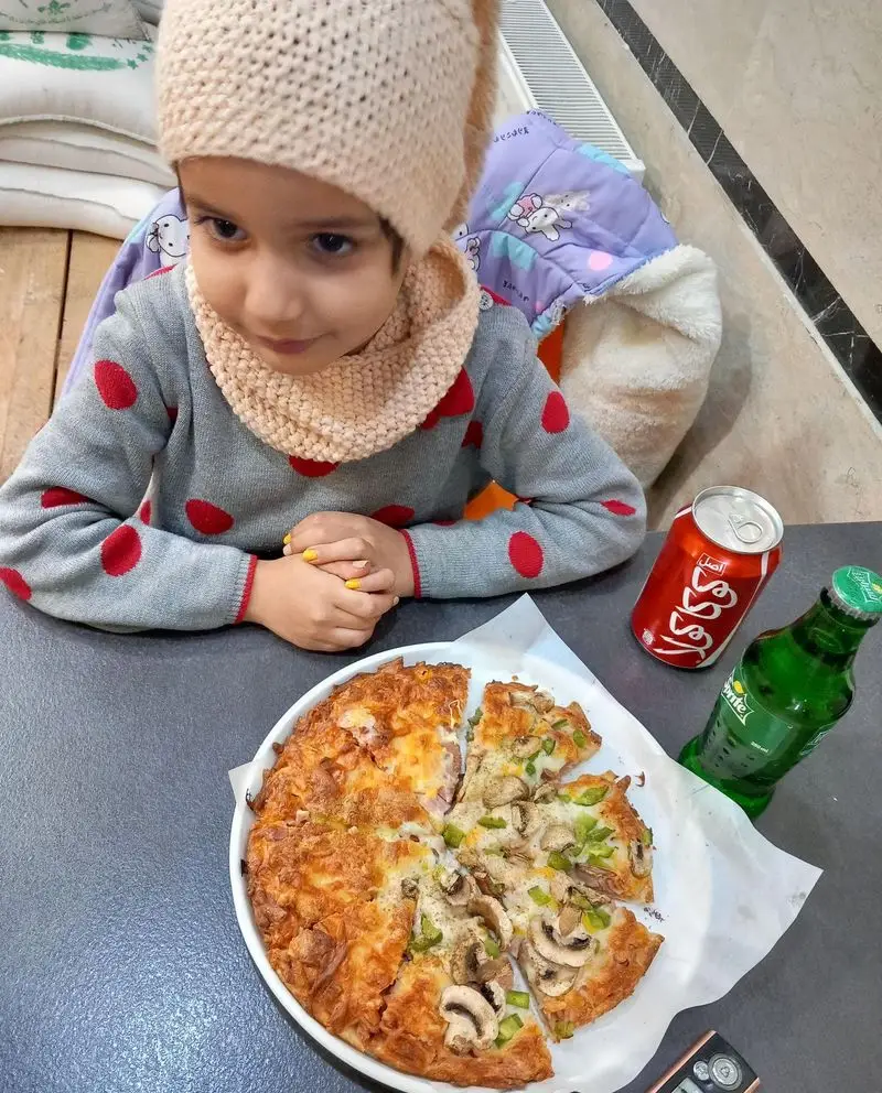تصویری از یک دختربچه دوست داشتنی در فستفود گل رز، لذت بردن از پیتزا قارچ و سبزیجات تازه، همراه با نوشیدنی‌های کوکاکولا و اسپرایت.