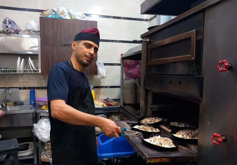 آشپز فستفود گل رز در حال پخت کباب ترکی با قارچ و تهیه ساندویچ‌های تازه در فر صنعتی آشپزخانه رستوران.