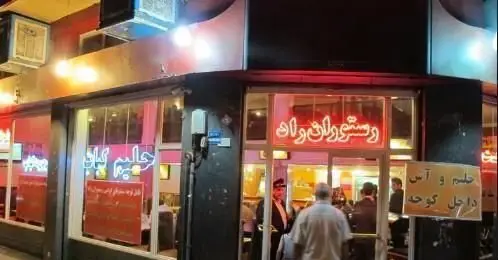 تصویر شبانه کسب و کار "آش و حلیم پزی راد" با تابلوهای نئونی "رستوران راد" و "حلیم و آش" و مشتریان در حال ورود.