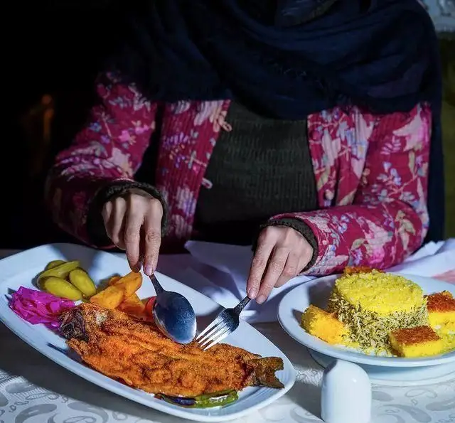 مشتری در حال میل کردن ماهی سرخ شده با پلو زعفرانی و ترشی در رستوران سنتی ترمه؛ لذت غذای اصیل ایرانی.