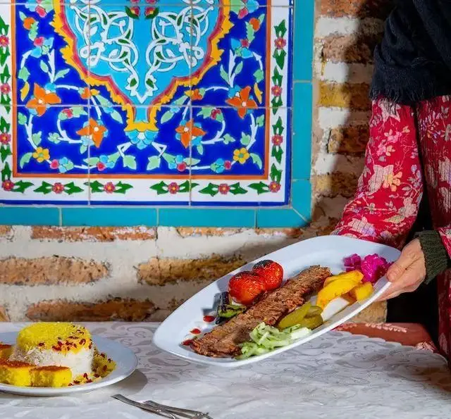 سرو چلو کباب کوبیده با گوجه و ترشی در رستوران سنتی ترمه با محیطی دلنشین و کاشی‌کاری‌های زیبا، غذای ایرانی اصیل