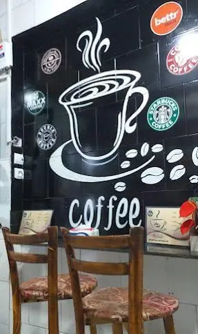 کافه قهوه سنتر: دیواری سیاه با نقاشی فنجان قهوه سفید، بخار، دانههای قهوه، کلمه "coffee" و لوگو استارباکس و سایر برندها. صندلیهای چوبی.