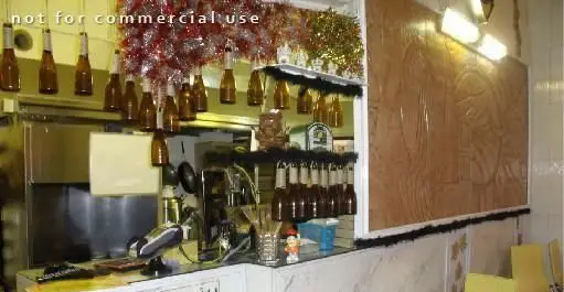 فست فود ماه تولد: نمای داخلی با پیشخوان پر از تجهیزات، بطری‌های آویزان دکوراتیو، تزئینات جشن و دیوار برجسته طرح‌دار