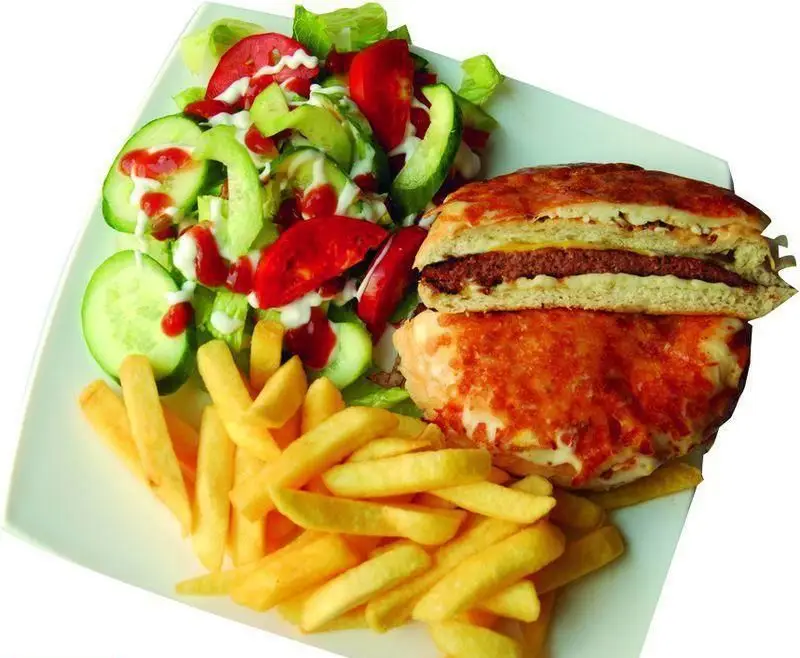 بشقاب فست فود از پیتزا دومینو جردن: برگر با نان پخته و پنیر، سیب زمینی سرخ کرده طلایی و سالاد سبزیجات تازه با سس. منوی متنوع رستوران.