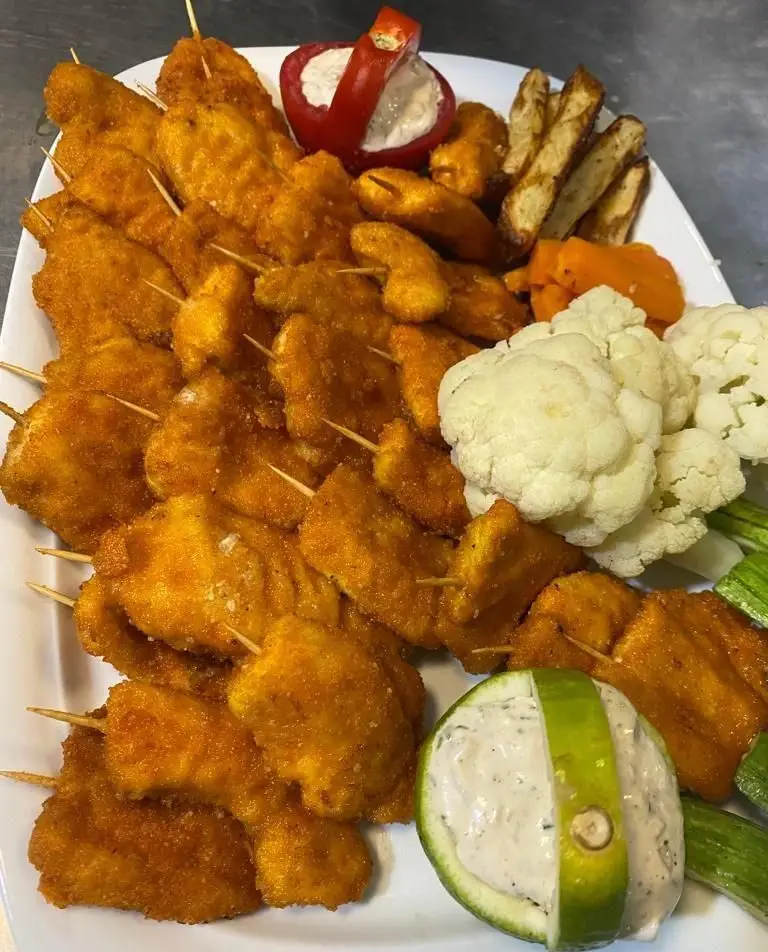 سینی بزرگ و جذاب کترینگ لاوان شامل سیخ‌های جوجه سوخاری طلایی، سیب زمینی سرخ‌شده، کلم گل و سس‌های مخصوص برای پذیرایی مجالس.