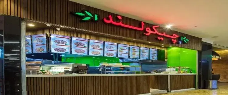 تصویر نمای بیرونی شیک فست فود چیکولند، دارای دکوراسیون چوبی و تابلوی نئون قرمز با لوگوی برگ سبز، همراه با منوی دیجیتال در یک محیط مدرن.