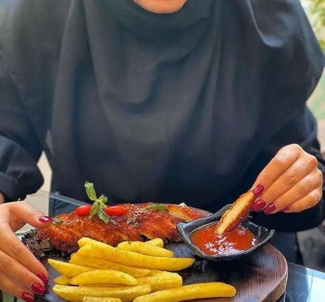 مشتری در کافه چوب سبز، از غذای شنیتسل یا ماهی سوخاری با سیب‌زمینی سرخ‌کرده و سس لذت می‌برد. تجربه طعم عالی در فضای دلنشین کافه چوب سبز.