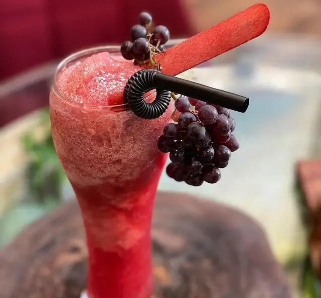نوشیدنی اسموتی قرمز رنگ و خوشمزه با تزیین انگور تازه و نی در لیوان بلند، مناسب برای روزهای گرم در کافه چوب سبز.
