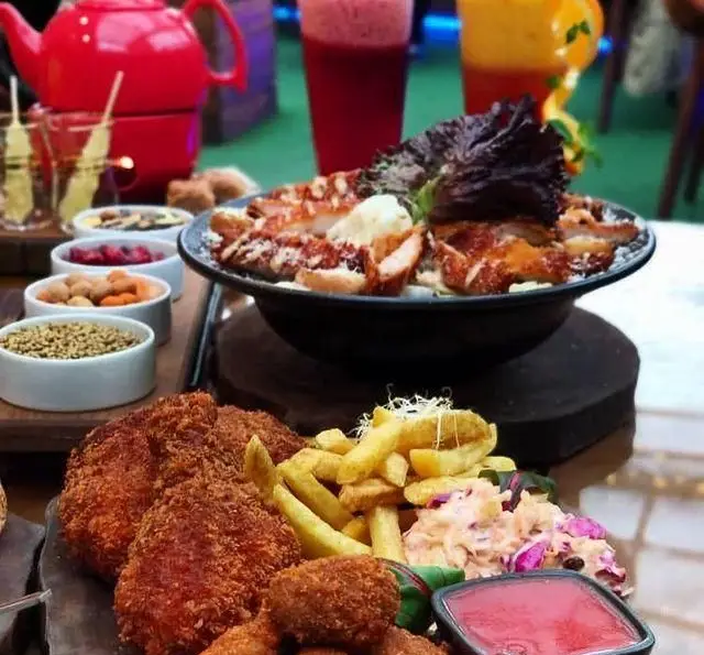 تصویری از میز غذا در کافه چوب سبز با مرغ سوخاری، سیب‌زمینی، سالاد، نوشیدنی‌های رنگارنگ و چای گرم.