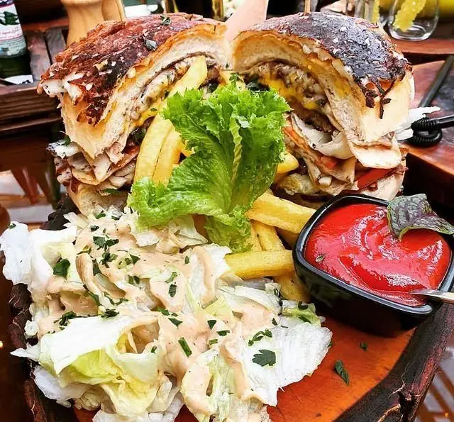 میز غذای کافه چوب سبز: دو برگر بزرگ و پرملات، همراه با سیب‌زمینی سرخ‌کرده، سالاد سبز تازه و کاسه سس کچاپ خوش‌رنگ.