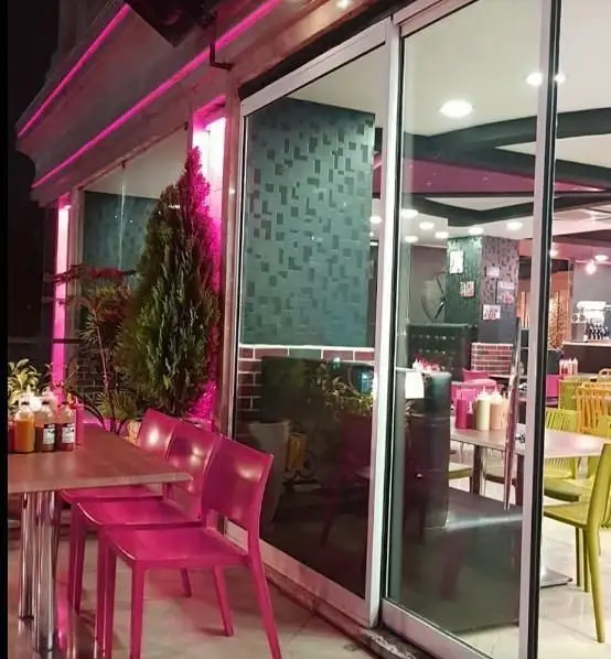 نمای شیک رستوران پیتزا ناخدا در شب، با صندلی‌های صورتی در فضای باز و نورپردازی نئون جذاب، میزبان مشتریان پیتزا و فست‌فود.