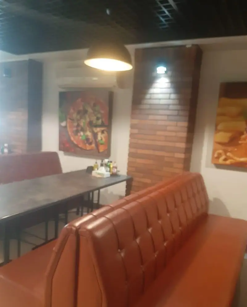 فضای داخلی رستوران بیگ بنگ با دکوراسیون مدرن، شامل میزهای غذاخوری و نیمکت‌های چرمی راحت، همراه با نقاشی‌های جذاب غذا روی دیوار.