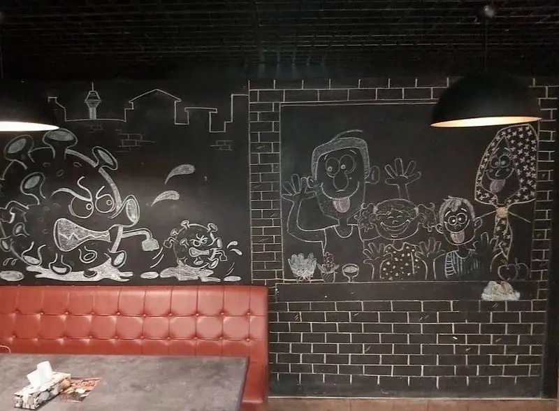 دکوراسیون داخلی رستوران بیگ بنگ با نقاشی های گچی خلاقانه روی دیوار، شامل طرحی طنزآمیز از ویروس کرونا و شخصیت های کارتونی.