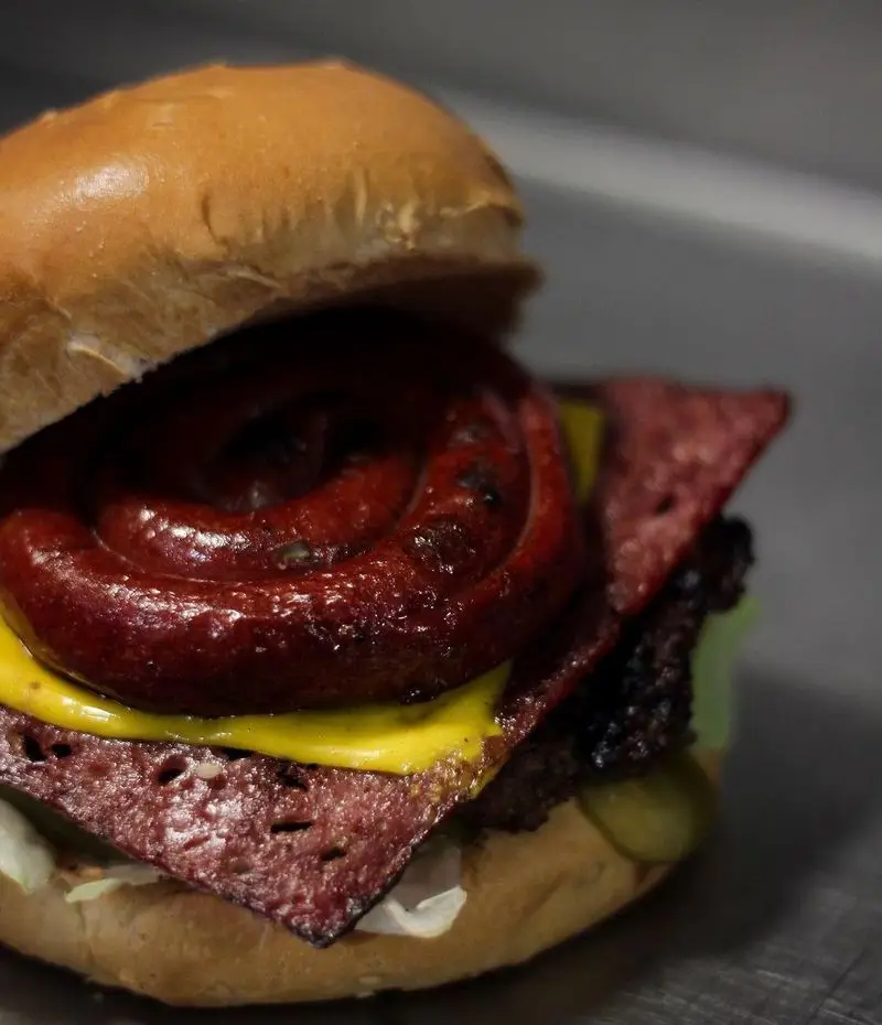 همبرگر مخصوص رستوران بیگ بنگ با سوسیس حلزونی کبابی، ورقه‌های پاسترامی، پنیر آب شده، گوشت و نان برگر.