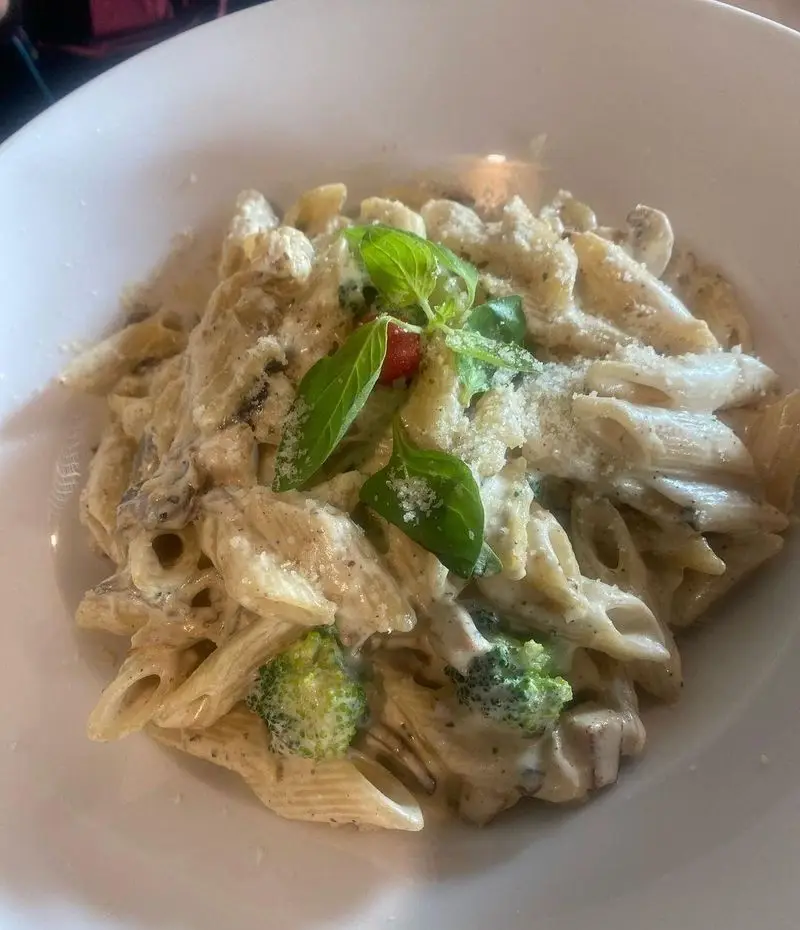 پاستا پنه با سس آلفردو خامه ای، قارچ و بروکلی تازه، تزئین شده با پنیر و ریحان در رستوران بیگ بنگ، غذای لذیذ ایتالیایی.