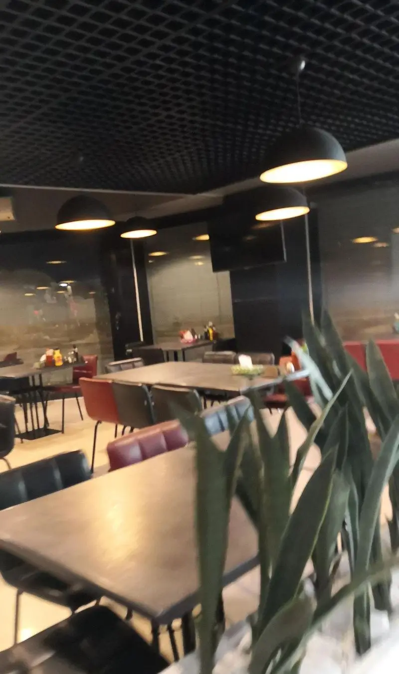 فضای داخلی دلباز و شیک رستوران بیگ بنگ، با طراحی مدرن شامل سقف مشبک، میز و صندلی‌های راحت و نورپردازی گرم و دلپذیر.