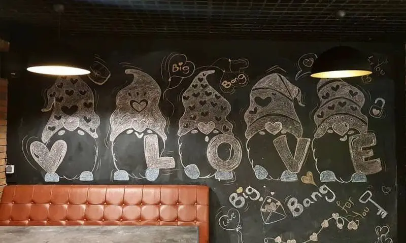 دیوار گچی رستوران بیگ بنگ مزین به نقاشی گنوم‌های قلب‌دار و کلمه LOVE، همراه با نیمکت چرمی قهوه‌ای برای فضایی دلنشین و رمانتیک.
