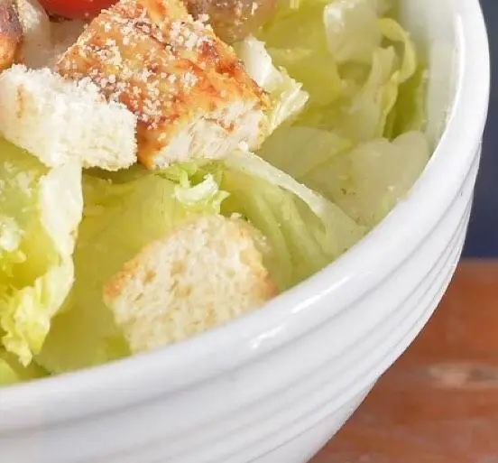 نمای نزدیک از یک سالاد سزار لذیذ با مرغ گریل طلایی، کاهوی تازه و کروتون‌های ترد در کاسه سفید رستوران باغ طهرون.