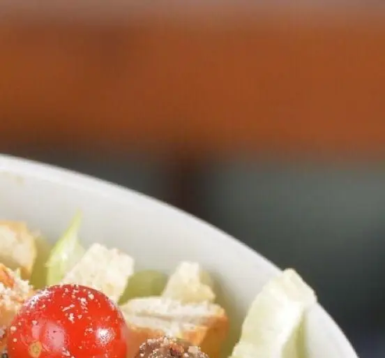 تصویری نزدیک از سالاد سزار خوش‌طعم و تازه با گوجه گیلاسی و کروتون در رستوران باغ طهرون. پیش غذایی لذیذ.