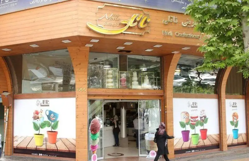 نمای بیرونی قنادی ناتلی با تابلوی زردرنگ، ویترین کیک‌های زیبا و بستنی‌های رنگارنگ، دکوراسیون چوبی و درب ورودی شیشه‌ای.