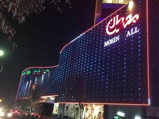 مرکز خرید معین مال در شب با نورپردازی آبی و قرمز خیره‌کننده و تابلوی درخشان "MOEIN ALL"، مقصدی جذاب برای بازدیدکنندگان.